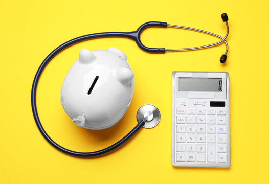 Piggy bank, calculator and stethoscope on yellow background, flat lay. Medical insurance
