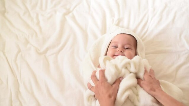 Baby with blue eyes in white towel after bath lies on back. Hands of mother caress of kid. copy space for text. First year of life and hygiene of child. happy and exited newborn baby.