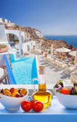 Greek food against luxury resort with swimming pool in Oia village on Santorini island in Greece