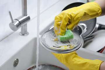 Woman washing dirty dishes in kitchen sink, closeup