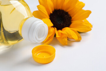 Bottle of cooking oil and sunflower on white table, closeup