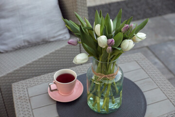 Beautiful bouquet of colorful tulips and cup with drink on rattan garden table outdoors