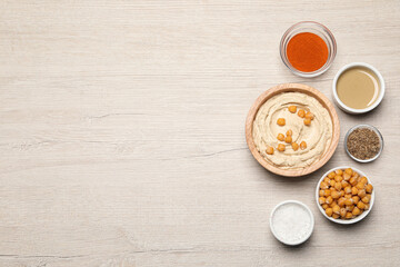 Bowl with delicious hummus and different ingredients on white wooden table, flat lay. Space for text