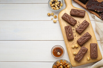Delicious chocolate candy bars, caramel and nuts on white wooden table, flat lay. Space for text