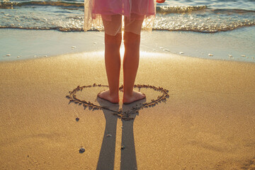 A little girl stands in the heart on the sunny beach. From the beach holiday with love.