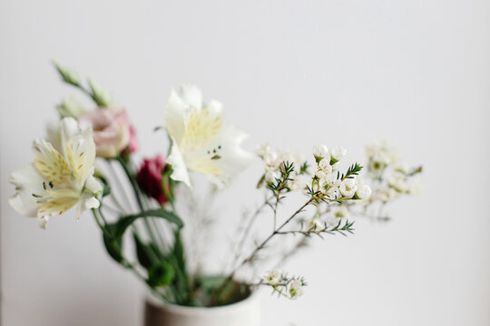 Stylish bouquet in ceramic vase at window, moody image. Beautiful fresh flowers, manuka, alstroemeria, eustoma, eucalyptus floral arrangement. Spring modern bouquet close up