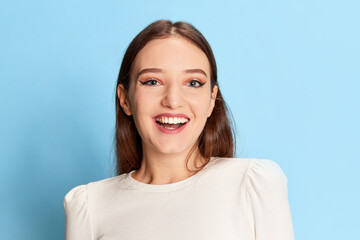 Obraz premium Portrait of young beautiful girl in casual clothes posing, smiling over blue studio background. Concept of emotions, lifestyle, youth