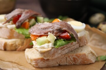 Fototapeta na wymiar Delicious bruschettas with anchovies, eggs, cream cheese, tomatoes, bell peppers and cucumbers on parchment, closeup