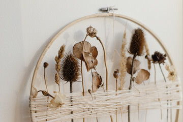 Stylish boho autumn wreath with dry flowers. Wooden hoop, thread and dry herbs on white wall...
