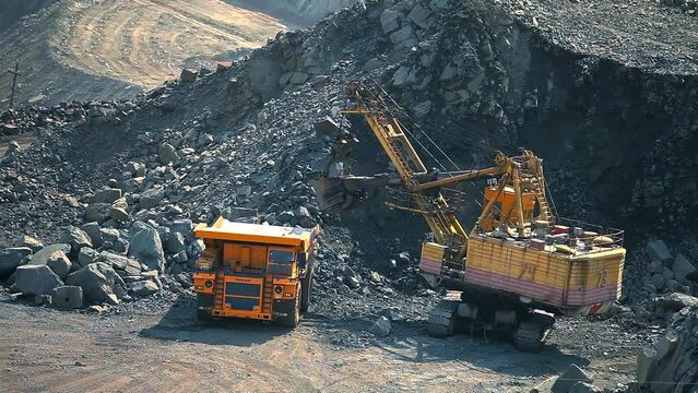 An excavator in a quarry loads soil into a dump truck. Equipment for the extraction of iron ore in an open pit. A large mining excavator is loading a mining truck in an iron ore quarry.