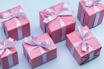 A set of gift boxes wrapped in pink paper tied with a lilac satin ribbon. Blue background, studio shot.