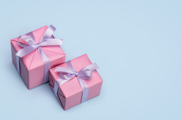 Two stylish gift boxes wrapped in pink paper, decorated with a lilac satin ribbon. Blue background, copy space.