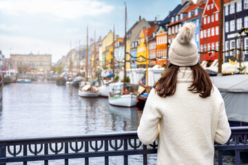A tourist woman in winter clothing enjoys the view to the beautiful Nyhavn area in Copenhagen, Denmark, during winter time
