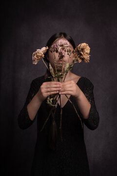 studio portrait of a womand in black dress holding dried flowers in front of her face