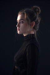 Profile portrait of a young woman, wear black suitcase, over black background.