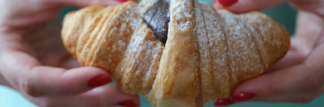 Hand shows a fresh croissant with chocolate and powdered sugar