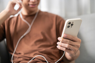 Relaxed young asian man music lover sitting listening music on earphones. Man holding mobile phone in living room listening to music with headphones and mobile phone