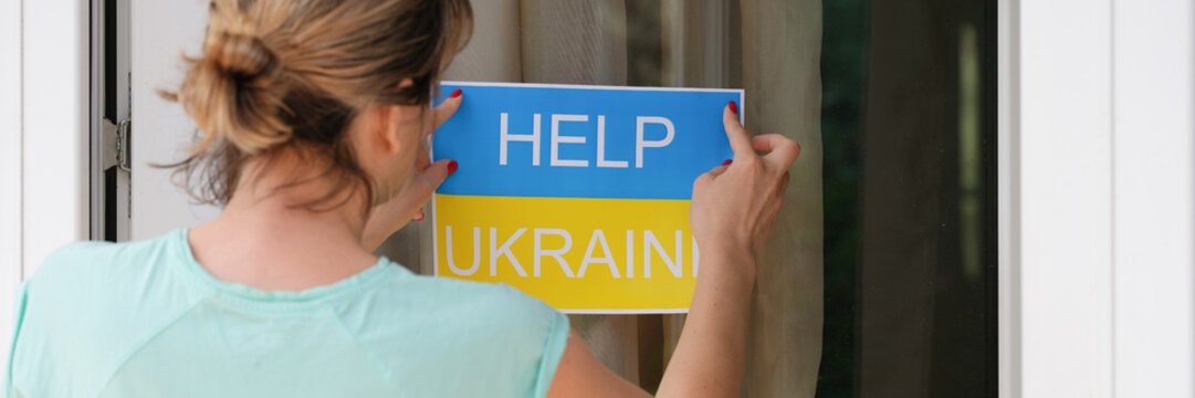 Woman glues banner on glass with the text help to Ukraine