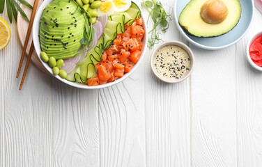 Delicious poke bowl with avocado, fish and edamame beans on white wooden table, flat lay. Space for text