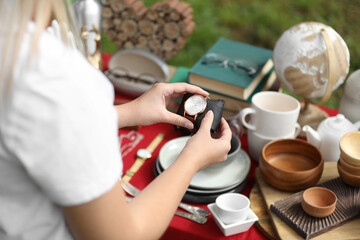 Woman holding beautiful watch near table with different items on garage sale, closeup