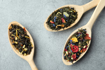 Different kinds of dry herbal tea in wooden spoons on light grey table, flat lay