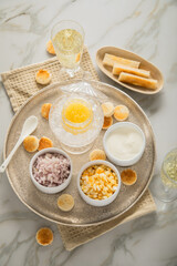 Gelber Saiblings Kaviar auf Eis in Glas Schale mit Porzellan Löffel, gekochte Eier Würfel, Charlotten Zwiebel Würfel, Toast Brot, Saure Sahne und Champagner Sekt auf Silber Teller und Marmor hell
