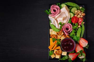 Antipasto platter cold sliced ham, salami, crackers, strawberries, vegetables and cheese platter on  board over dark background. Appetizers table with italian antipasti snacks. Top view