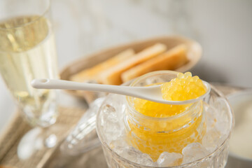 Gelber Saiblings Kaviar auf Porzellan Löffel mit Toast Brot und Champagner Sekt auf Eis, Silber Teller und Marmor hell