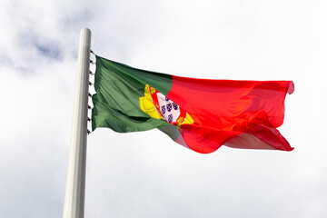 A large flag of Portugal is flying in a strong wind in cloudy sky