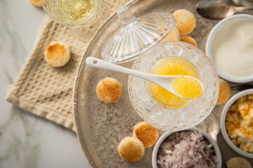 Gelber Saiblings Kaviar auf Eis in Glas Schale mit Porzellan Löffel, gekochte Eier Würfel,...