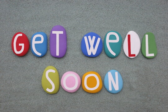 Get well soon, creative message composed with multi colored stone letters over green sand