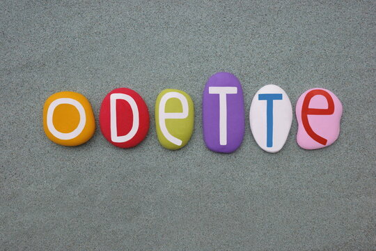 Odette, female given name composed with multi colored stone letters over green sand