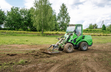 A green mini skid steer loader clear the construction site. Land work by the territory improvement....
