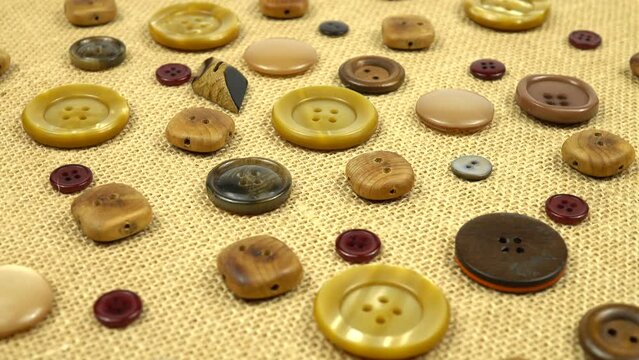 Brown buttons in different designs and sizes for sewing on clothes lie on burlap. 