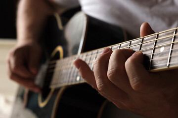 Obraz premium Playing the guitar. Strumming acoustic guitar. Musician plays music. Man fingers holding mediator. Man hand playing guitar neck in dark room. Unrecognizable person rehearsing, fretboard close-up.