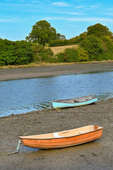 Two wooden rowing boats on the shore of an estuary ay loew tide. No people.