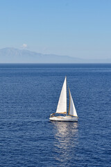 Fototapeta premium Sailing yacht with white sail on a calm sea with coastline in the background