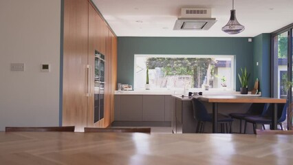 Camera tracks interior of beautiful contemporary kitchen with fitted appliances and storage with views to garden - shot in slow motion