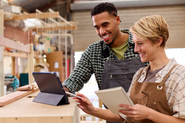 Male And Female Apprentices With Digital Tablet Working As Carpenters In Furniture Workshop