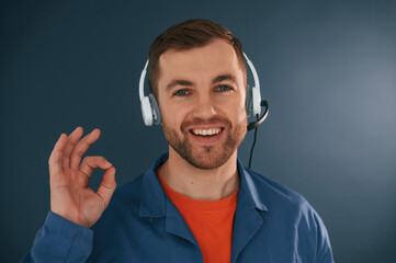 Showing fine, okay, good, sign. Smiling. In headphones. Handsome man is in the studio against blue background