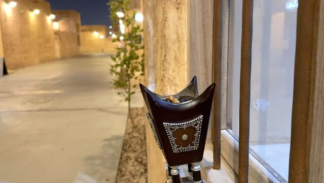Arabian Bakhoor incense burner censer with smoke and blurred background of old city down town in Doha Qatar Al Wakrah Souq with gold luxurious lighting renovation houses to visit at night walk family