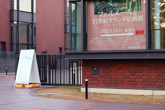 TOKYO, JAPAN - December 15, 2021: Window of Tokyo Metropolitan Art Museum with  poster advertising upcoming exhibition. Notice board with information on coronavirus-related safety measures is by it.