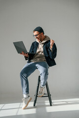 In casual clothes. With laptop. Sitting on the chair. Handsome man is in the studio against white background
