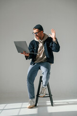 In casual clothes. With laptop. Sitting on the chair. Handsome man is in the studio against white background