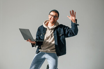 In casual clothes. With laptop. Sitting on the chair. Handsome man is in the studio against white background