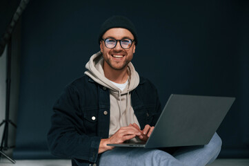 Using laptop and smiling. Handsome man is in the studio against background