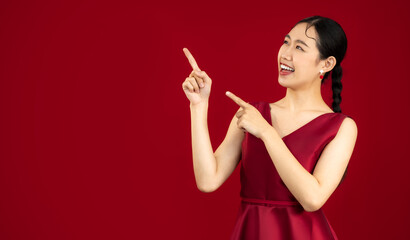 Asian woman in red elegant silk dress pose smiling and fingers pointing up to your text red background.