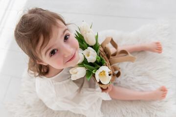 Top view close-up portrait of little girl in a white dress, nightgown. Toddler embraces a bouquet...