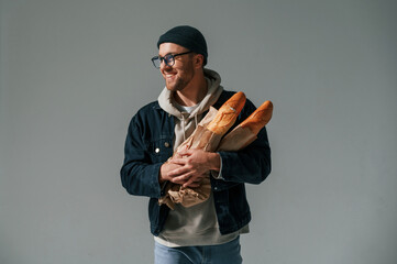 With bunch of baguettes in hands. Handsome man is in the studio against white background
