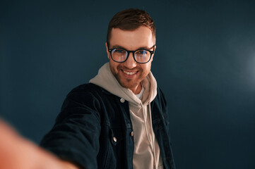 Making selfie. Handsome man is in the studio against blue background